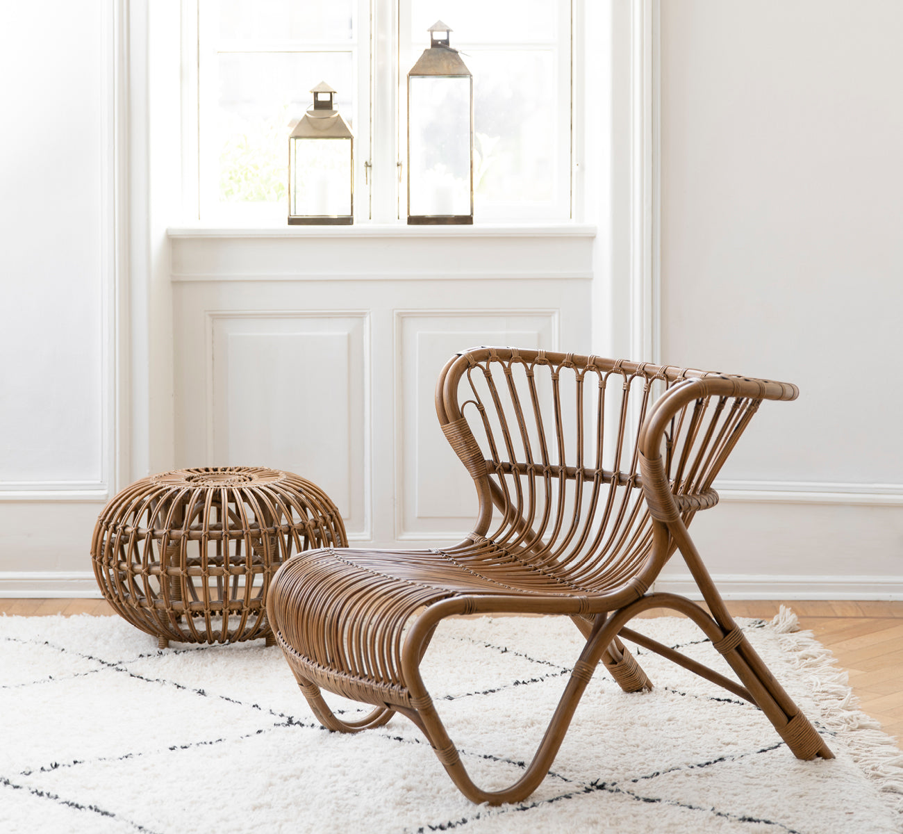 Dette er et livsstilsbillede af Fox Lænestol i polished Antique Rattan, i et varmt interiør med okkerfarvet lambrisering og mørkt sildebensgulv.