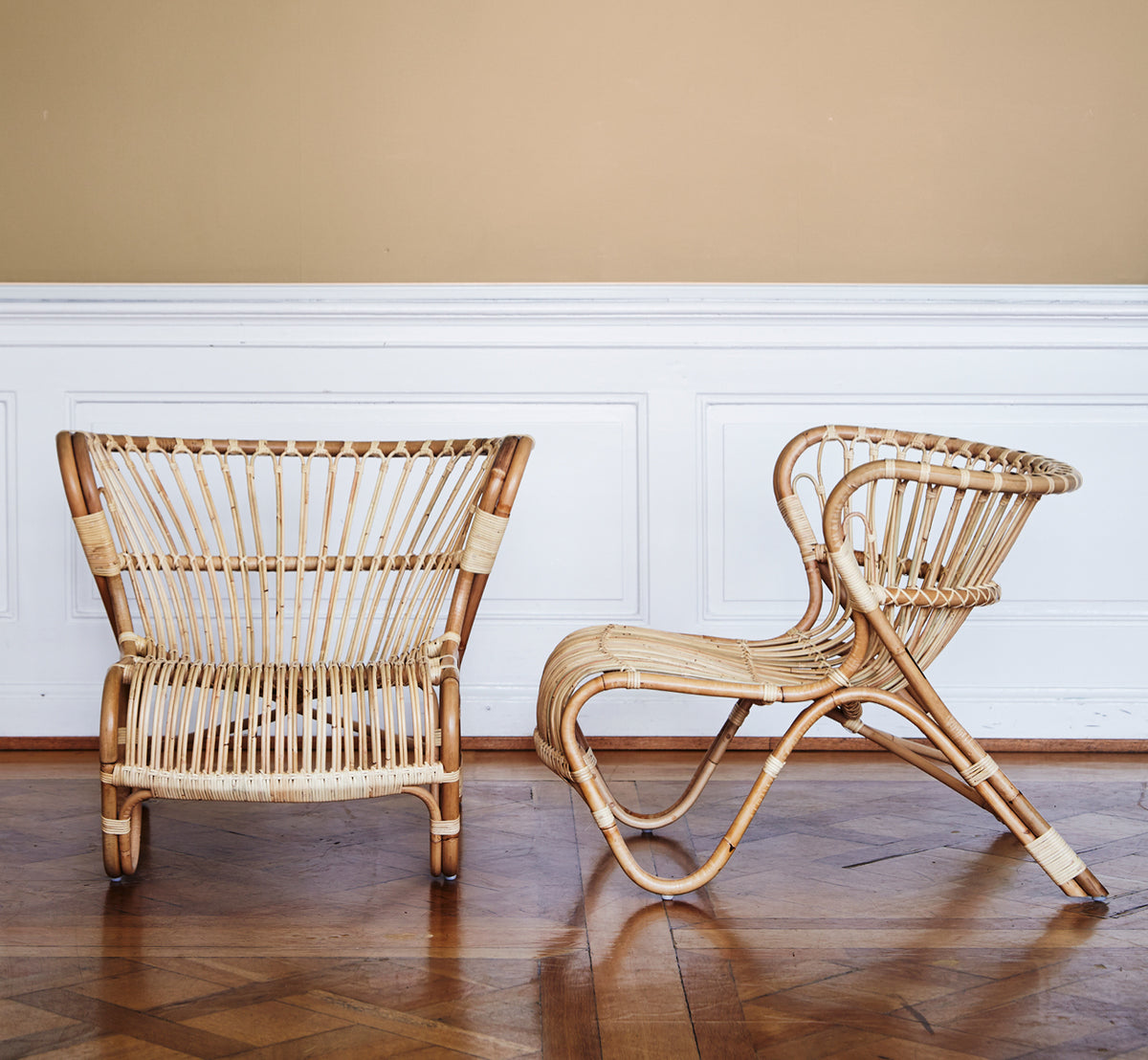 Dette er et livsstilsbillede af Fox Lænestol i polished Natural Rattan, i et varmt interiør med okkerfarvet lambrisering og mørkt sildebensgulv.