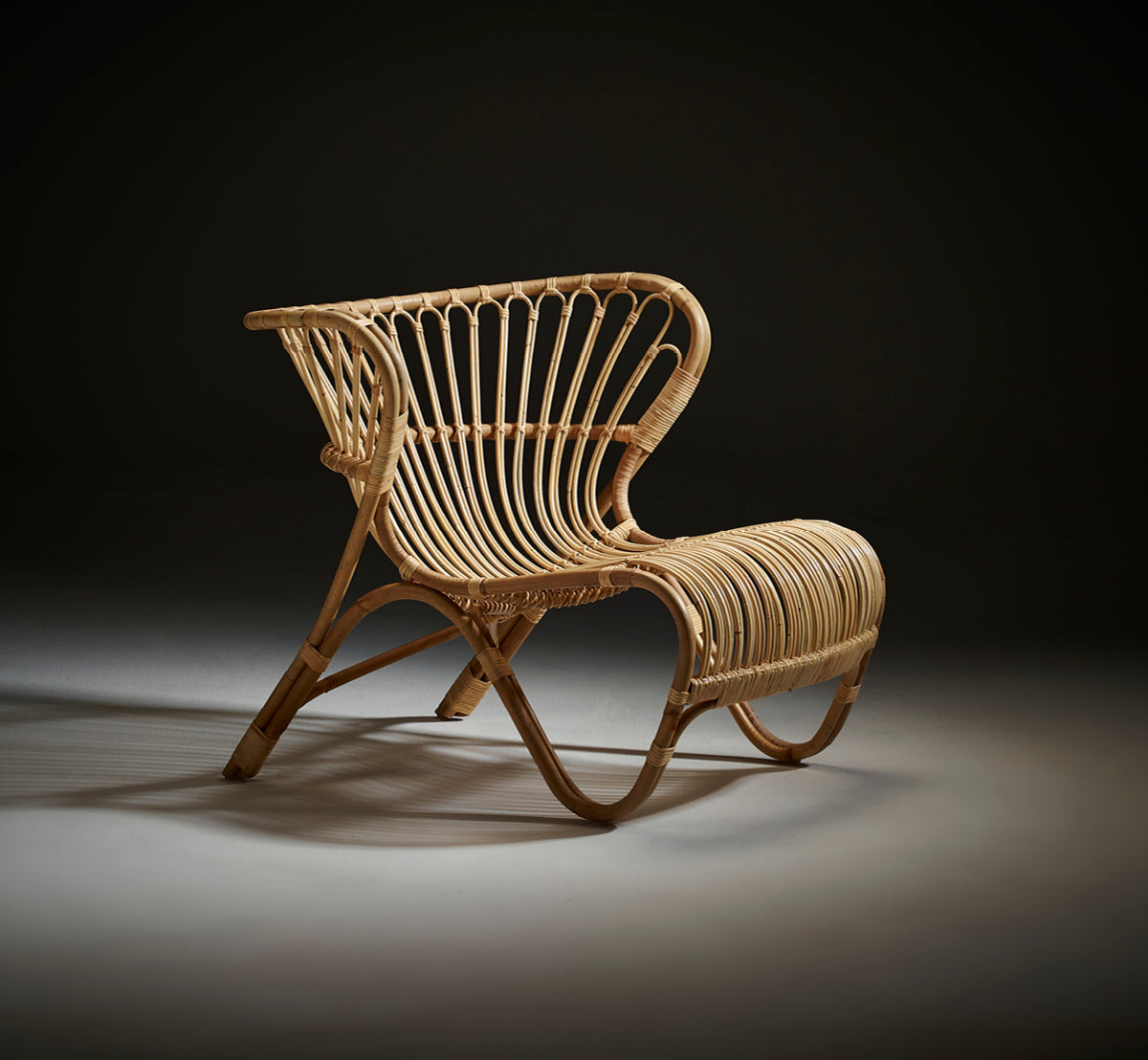 Dette er et livsstilsbillede af Fox Lænestol i polished Natural Rattan, i et varmt interiør med okkerfarvet lambrisering og mørkt sildebensgulv.