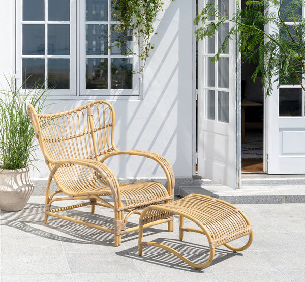 Dette er et livsstilsbillede af Teddy Udendørs fodskammel i natural aluminium artfibre. Kombineret med den matchende lænestol på en solbeskinnet brolagt terrasse.