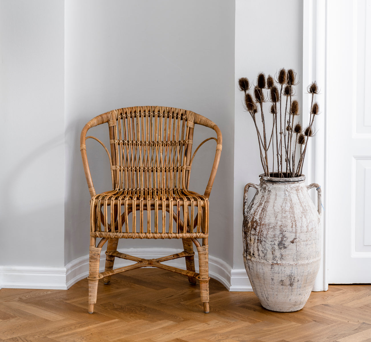 Dette er et livsstilsbillede af Robert Spisebordsstol i polished antique rattan. Placeret ved siden af en høj terrakotta-urne på et sildebensparketgulv.