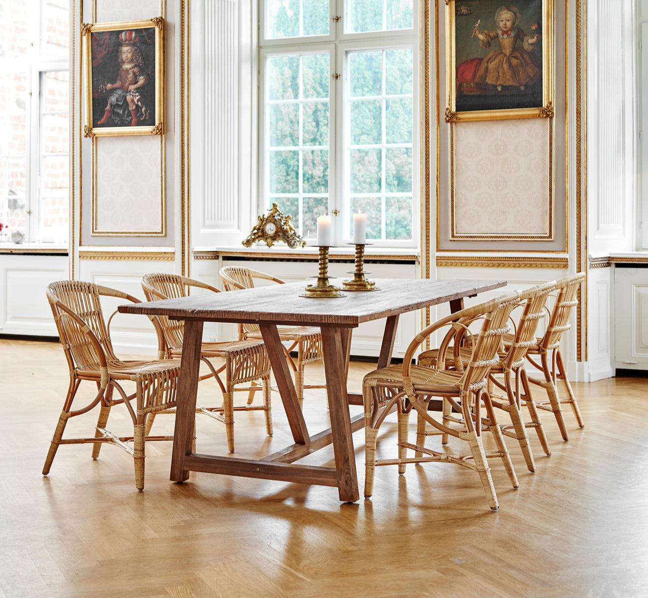 Dette er et livsstilsbillede af Robert Spisebordsstol i polished antique rattan. Placeret ved siden af en høj terrakotta-urne på et sildebensparketgulv.