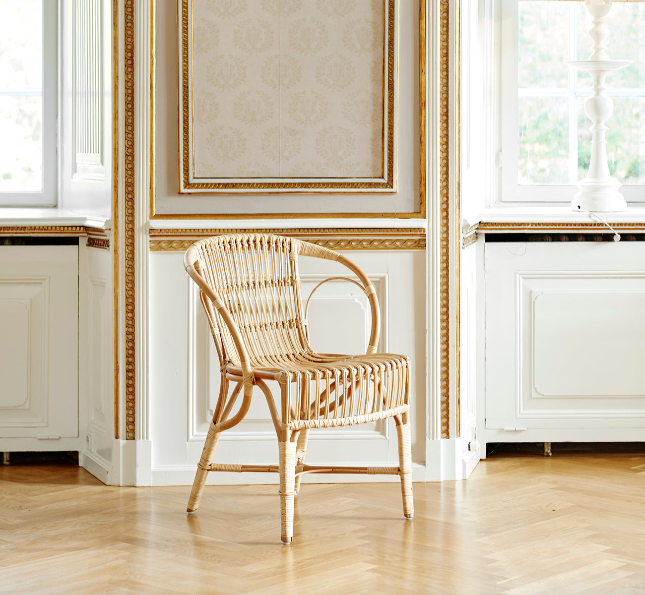 Dette er et livsstilsbillede af Robert Spisebordsstol i polished natural rattan. Placeret ved siden af et søjlebord med tulipaner på et jutetæppe.