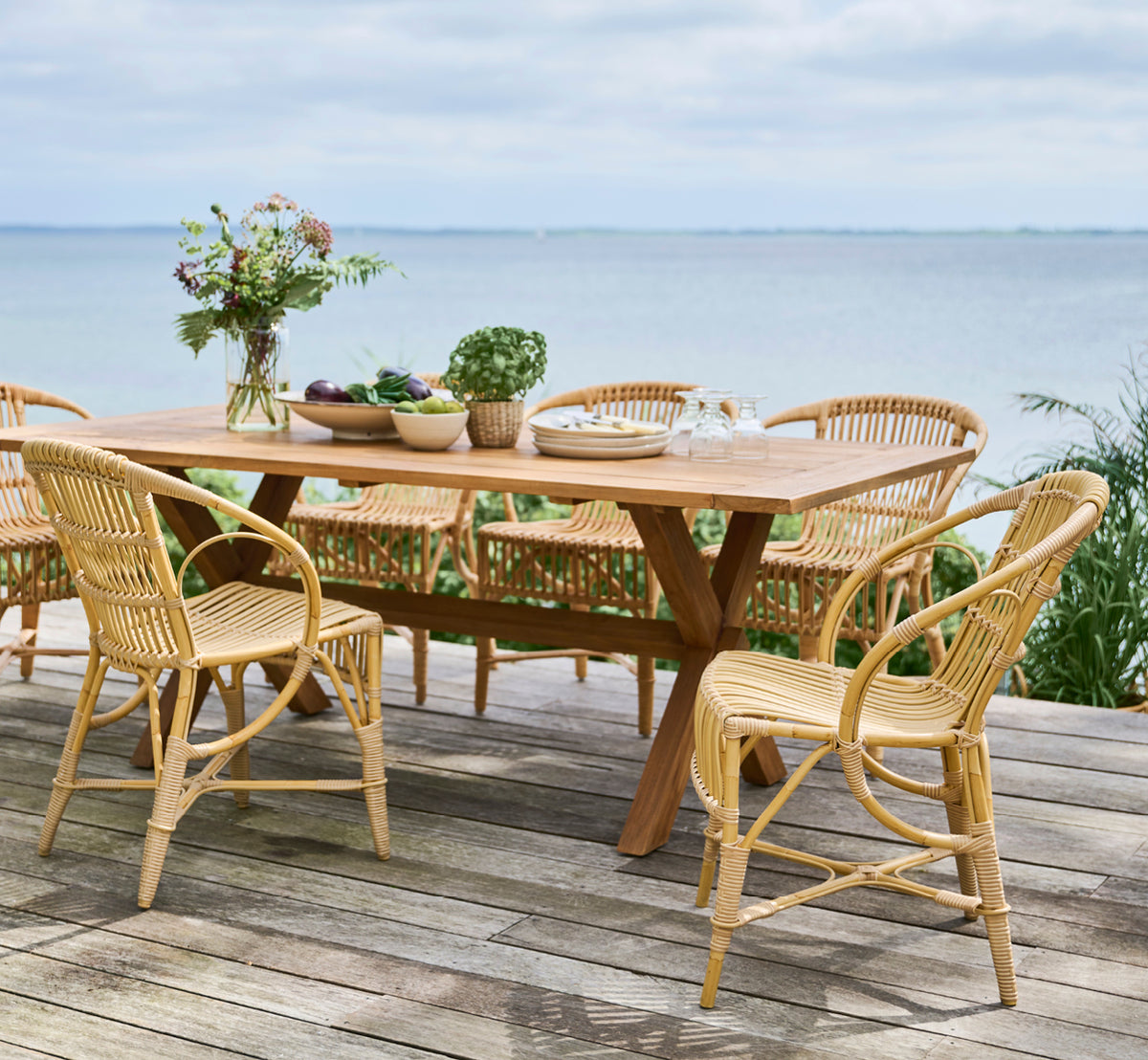 Dette er et livsstilsbillede af Robert Udendørs spisebordsstol i natural aluminium artfibre. Opstillet omkring et teakbord på et trædæk med udsigt over havet.