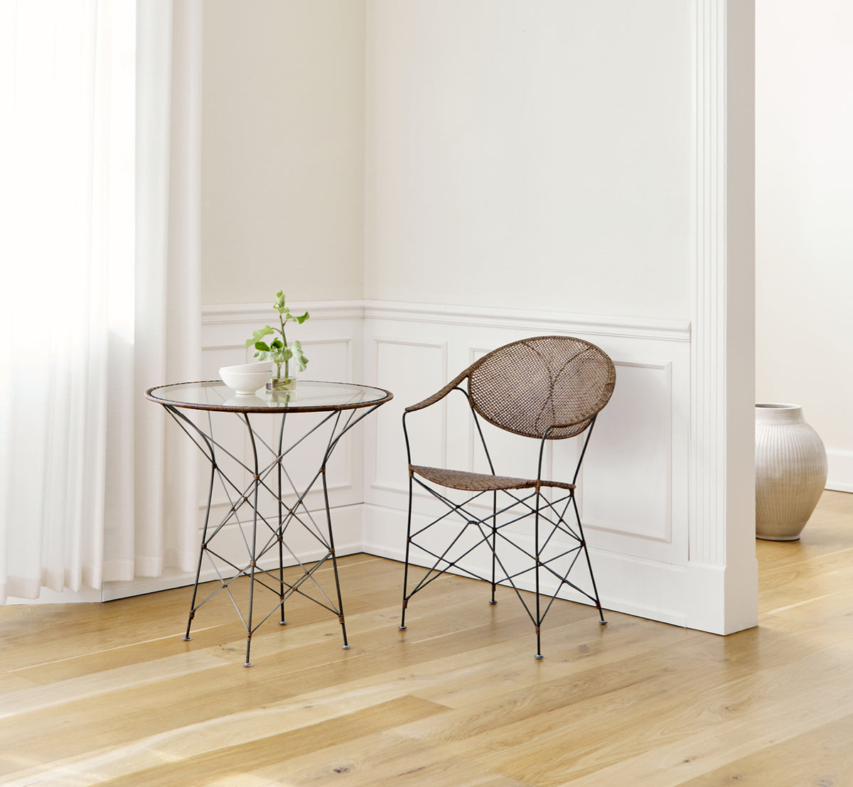 Dette er et livsstilsbillede af Funky Spisebordsstol i hazelnut rattan iron frame, i et lyst interiør med hvide panelvægge og sildebensgulv.