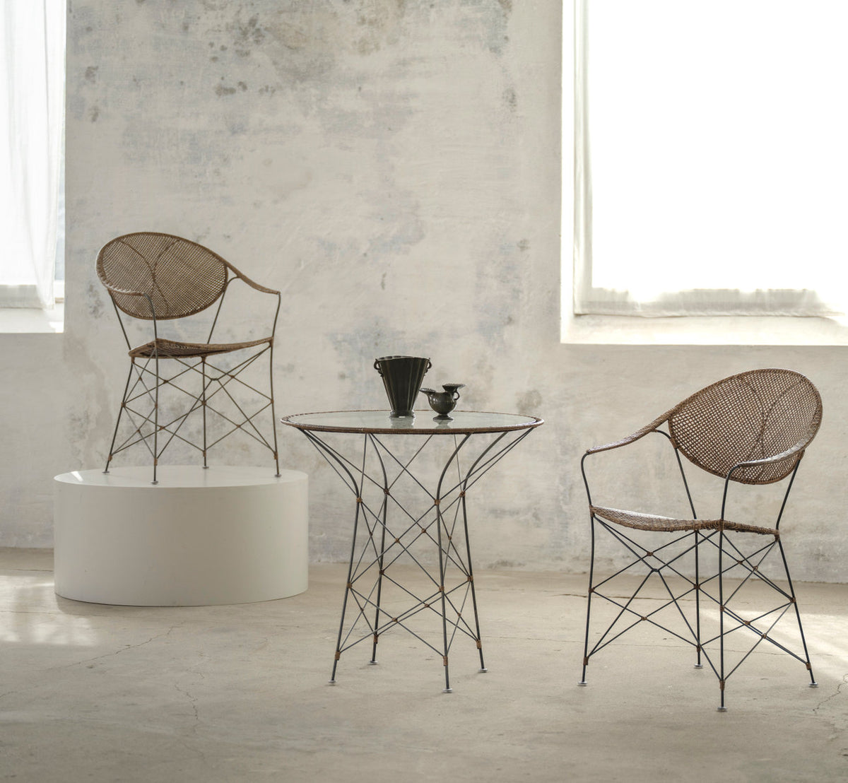 Dette er et livsstilsbillede af Funky Cafébord i hazelnut rattan iron frame. Med stole og en sokkel i et lyst rum.