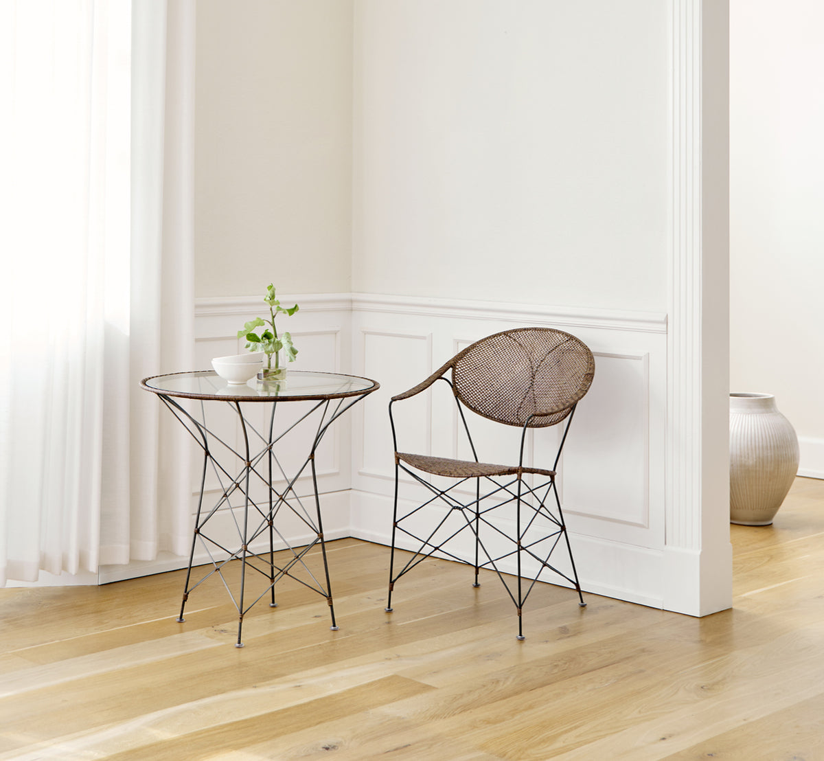 Dette er et livsstilsbillede af Funky Spisebordsstol i hazelnut rattan iron frame, i et lyst interiør med hvide panelvægge og sildebensgulv.